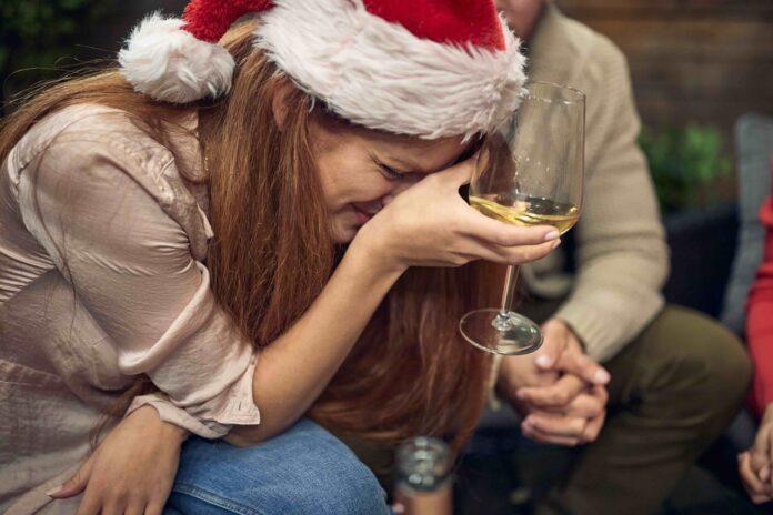 caucasian female holding glass of white wine, dying laughing, or crying, with santa hat